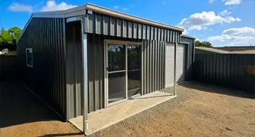 NBT Construction shed builder homepage image of a domestic granny flat syle shed in dark green with a verandah.